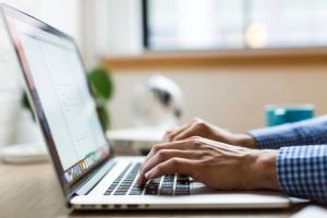 A man in a button-down shirt types on a laptop.