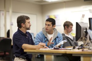 A student and instructor discuss a textbook in a computer lab 